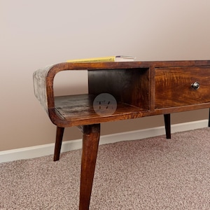 May include: A dark brown wooden coffee table with a curved shelf and a drawer. The table has four legs and is sitting on a light brown carpet.