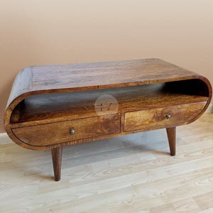 May include: A wooden coffee table with a curved top and two drawers. The table has a dark brown finish and is supported by four legs.