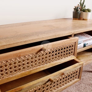 Pu&ograve; includere: Una consolle multimediale in legno con due cassetti con frontali in rattan intrecciato. La consolle ha mensole aperte sul lato destro e poggia su quattro gambe affusolate.