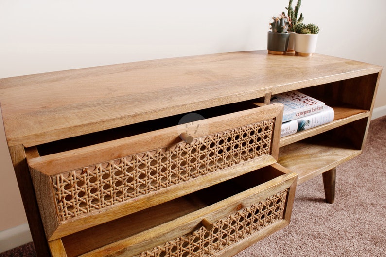 Pu&ograve; includere: Una consolle multimediale in legno con due cassetti con frontali in rattan intrecciato. La consolle ha mensole aperte sul lato destro e poggia su quattro gambe affusolate.
