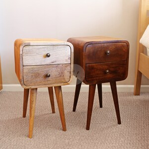 May include: Two wooden bedside tables with two drawers each. The tables have a rounded, curved front and are supported by four tapered legs. One table is a light wood tone and the other is a darker brown wood tone.