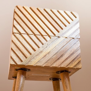 May include: A wooden side table with a geometric pattern on the top and four wooden legs. The table is made of light brown wood and has a natural finish.