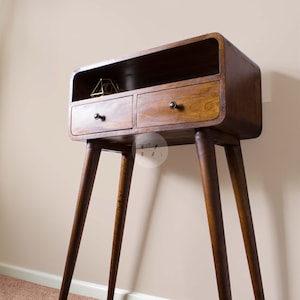 May include: A dark brown wooden console table with two drawers and a shelf. The table has a curved top and four tapered legs.