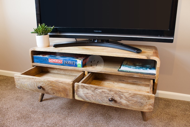 May include: A wooden TV stand with two drawers and a shelf. The drawers are open and the shelf is holding a board game and a book. The TV stand is on a carpet.