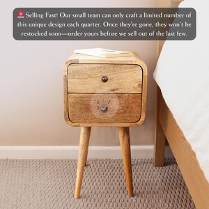 May include: A two-drawer wooden bedside table with rounded edges and tapered legs. The bedside table is made of light brown wood and has a natural finish. The drawers have metal knobs. "Selling Fast! Our small team can only craft a limited number of this unique design each quarter. Once they're gone, they won't be restocked soon-order yours before we sell out of the last few."