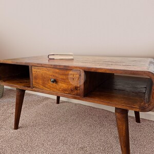 May include: A wooden coffee table with a drawer and open shelves. The table has a dark brown finish and is supported by four tapered legs.