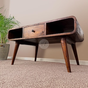 May include: A dark brown wooden coffee table with a curved design and a single drawer. The table has four legs with a mid-century modern style.