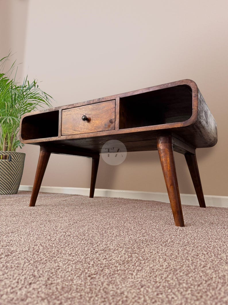 May include: A dark brown wooden coffee table with a curved design and a single drawer. The table has four legs with a mid-century modern style.