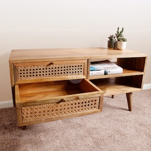Pu&ograve; includere: Un mobile TV in legno chiaro con due cassetti e due ripiani. I cassetti hanno una parte anteriore in rattan intrecciato. Il mobile ha un design moderno con gambe affusolate.