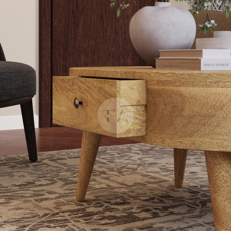 May include: A wooden coffee table with a rounded shape and a single drawer. The table has a light brown finish and four legs.