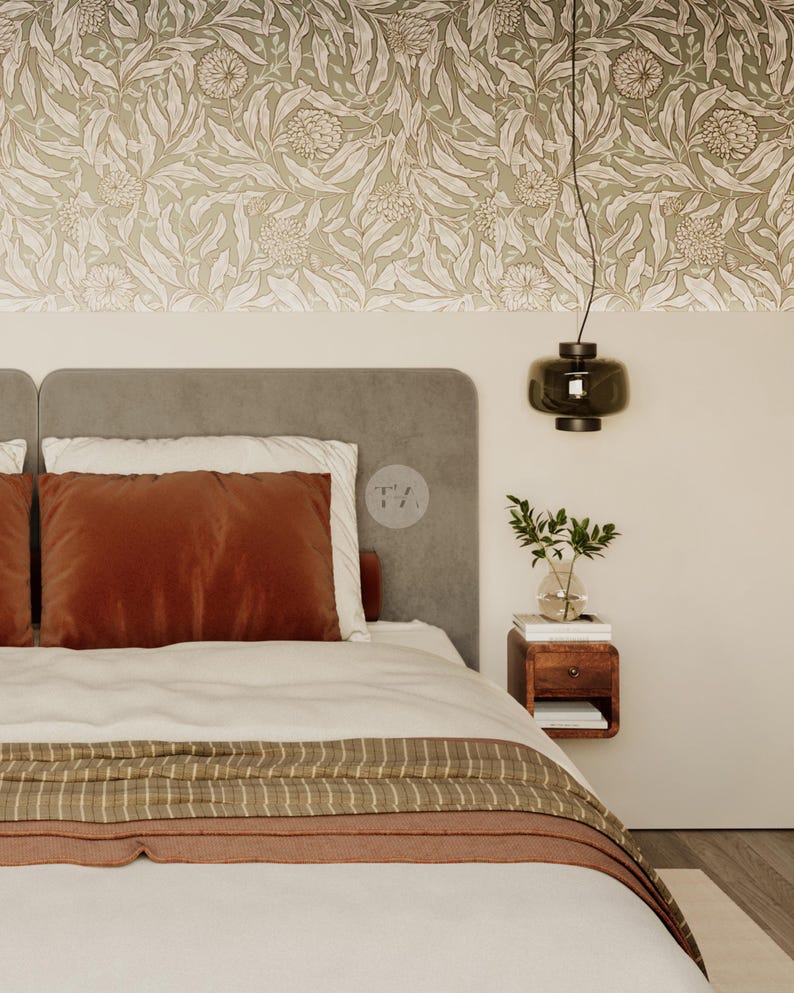 May include: A bedroom scene featuring a bed with a rust-colored velvet pillow and a striped throw blanket. The headboard is gray, and the wall has a floral wallpaper design. A dark green pendant light hangs above a wooden nightstand with a vase of greenery.