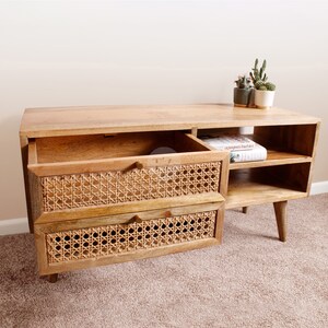 Pu&ograve; includere: Una consolle multimediale in legno chiaro con due cassetti in rattan e due ripiani aperti. La consolle ha un design moderno con gambe affusolate e una finitura in legno naturale.