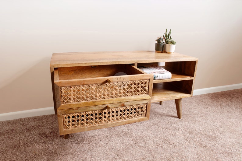 Pu&ograve; includere: Una consolle multimediale in legno chiaro con due cassetti in rattan e due ripiani aperti. La consolle ha un design moderno con gambe affusolate e una finitura in legno naturale.