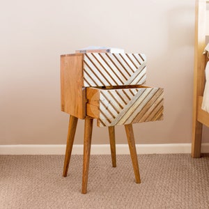 May include: A wooden bedside table with two drawers. The drawers have a geometric pattern of white and brown stripes. The table has four legs.