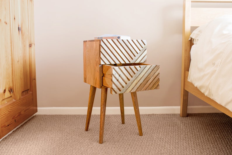 May include: A wooden bedside table with two drawers. The drawers have a geometric pattern of white and brown stripes. The table has four legs.