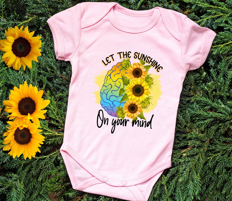 Puede incluir: Un body de beb&eacute; rosa con un gr&aacute;fico de cerebro arco&iacute;ris y el texto "Let the sunshine on your mind".
