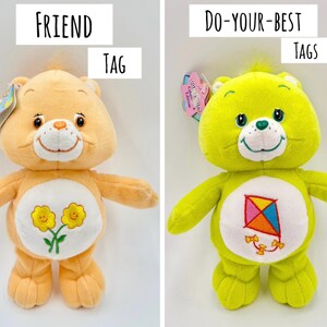 May include: Two plush bear toys with tags. The left bear is peach-colored with two yellow flowers on its belly. The right bear is lime green with a red and blue kite on its belly. Text labels read FRIEND TAG and DO-YOUR-BEST TAGS above each bear.