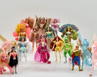 Op de afbeelding: Een verzameling van diverse fantasy-poppen en gevleugelde paardenfiguren. De poppen hebben verschillende haarkleuren, uitgebreide outfits met metallic accenten en capes. Twee gevleugelde paarden, een roze en een lichtblauwe, flankeren de groep poppen.