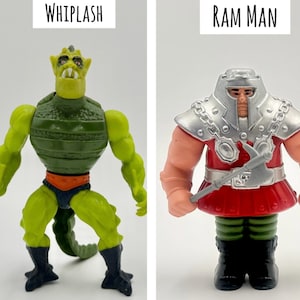 May include: Two action figures, "Whiplash" and "Ram Man", are displayed. Whiplash is green and yellow with a reptilian design, and the text "WHIPLASH" is above it. Ram Man is red, silver, and tan, with the text "RAM MAN" above it.