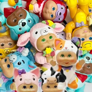Puede incluir: Una colección de figuras coloridas y caprichosas con disfraces de animales, como un perro, un cerdo, una vaca y un gato. Las figuras tienen ojos grandes y sostienen pequeños objetos como flores y conos de helado. La paleta de colores es pastel.