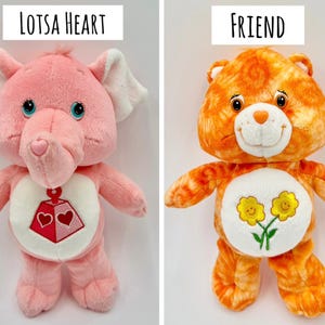 May include: Two plush toys. On the left, a pink elephant labeled LOTSA HEART with a red and pink heart-shaped toy emblem on its belly. On the right, an orange tie-dye bear labeled FRIEND with two yellow flowers on its white belly patch.