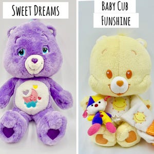 May include: Two plush bear toys. The left bear is purple with a white belly patch featuring a pink moon and blue cloud, labeled Sweet Dreams. The right bear is yellow with a white belly patch featuring a yellow sun, holding a small clown doll and a yellow blanket, labeled Baby Cub Funshine.