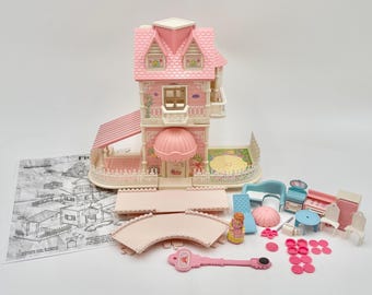 May include: A pink and white doll's house with a matching awning, balcony, and accessories. The set includes furniture, a key, and a doll. The doll's house has a pink roof and a detailed facade. Instructions are also included.