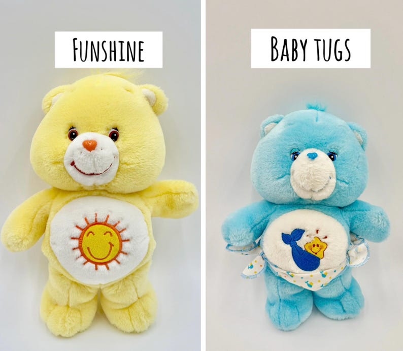 May include: Two plush bear toys. The left bear is yellow with a white belly patch featuring an orange sun with a smiling face and the text FUNSHINE above it. The right bear is light blue with a white belly patch showing a blue whale and a yellow star, wearing a patterned diaper with the text BABY TUGS above it.