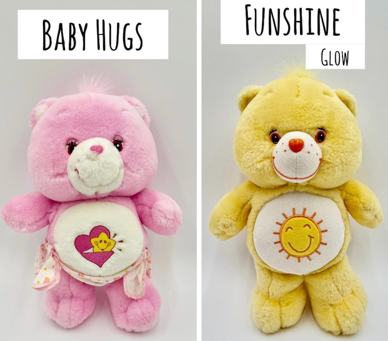 May include: Two plush bear toys. The left bear is pink with a white belly patch featuring a yellow star inside a pink heart and the text Baby Hugs. The right bear is yellow with a white belly patch featuring a yellow sun and the text Funshine Glow.