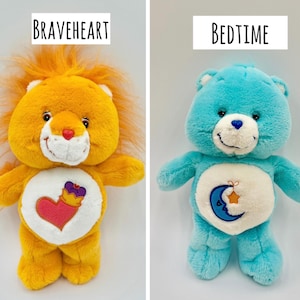 May include: Two plush toys labeled Braveheart and Bedtime. The orange Braveheart lion features a heart and crown emblem on its belly. The blue Bedtime bear features a crescent moon and star emblem on its belly. Both have white muzzles.