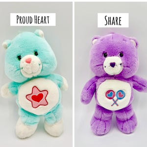 May include: Two plush bear toys. The left bear is light blue with a white belly patch featuring a red heart inside a pink star and the text Proud Heart. The right bear is purple with a white belly patch featuring two lollipops and the text Share.