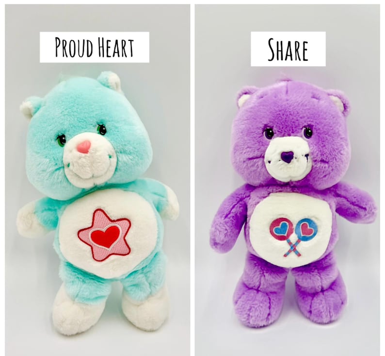 May include: Two plush bear toys. The left bear is light blue with a white belly patch featuring a red heart inside a pink star and the text Proud Heart. The right bear is purple with a white belly patch featuring two lollipops and the text Share.