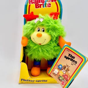 May include: A white ceramic mug with a black handle and the text "But First, Coffee" in a bold, black font. The mug is set against a blurred background, suggesting a cozy setting.