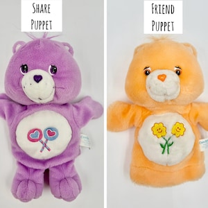 May include: Two plush hand puppets. The left is a purple bear with a white belly patch featuring two lollipops and the text Share Puppet. The right is an orange bear with a white belly patch featuring two yellow flowers and the text Friend Puppet.