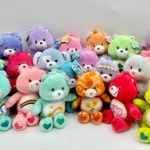 May include: A collection of various Care Bears plush toys in multiple colors including pink, blue, green, orange, purple, and red. Each stuffed animal features a unique embroidered belly badge, plastic nose, and attached product tags.