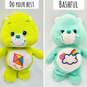 May include: Two plush bear toys. The left bear is lime green with a kite graphic on its belly and the text DO YOUR BEST above it. The right bear is mint green with a cloud and rainbow graphic on its belly and the text BASHFUL above it.