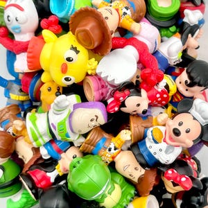 Può includere: Una collezione di colorate statuette Little People con vari personaggi. Le statuette includono personaggi come Batman, Mickey Mouse, Buzz Lightyear, Woody e Minnie Mouse. I giocattoli sono in vari colori, tra cui verde, giallo, rosso e blu.