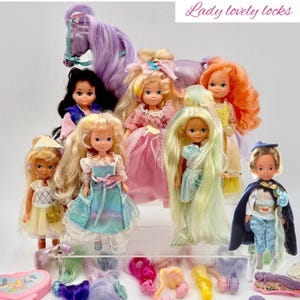 May include: A collection of vintage Lady Lovely Locks dolls and accessories. The dolls have long, colorful hair and wear various dresses. A purple horse with a long mane and tail is also present, along with extra hair pieces and a carrying case. The text "Lady lovely locks" is visible.