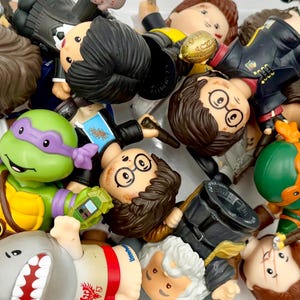 May include: A pile of plastic figurines, including a green Teenage Mutant Ninja Turtle, a shark, and figures resembling characters from the Harry Potter series. The figurines are in various poses and feature detailed designs.