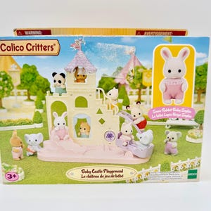 May include: A Calico Critters Baby Castle Playground playset. The box features a castle with various animal figures, including rabbits, pandas, and bears. The set includes a slide, stairs, and other playground elements. The box also features the text "Baby Castle Playground" and "Le château de jeu de bébé".
