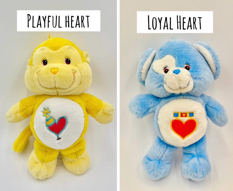 May include: Two plush toys: a yellow monkey labeled Playful Heart with a party hat and heart emblem on its belly, and a blue bear labeled Loyal Heart with a medal and heart emblem on its belly. Both have white belly patches and soft fur.