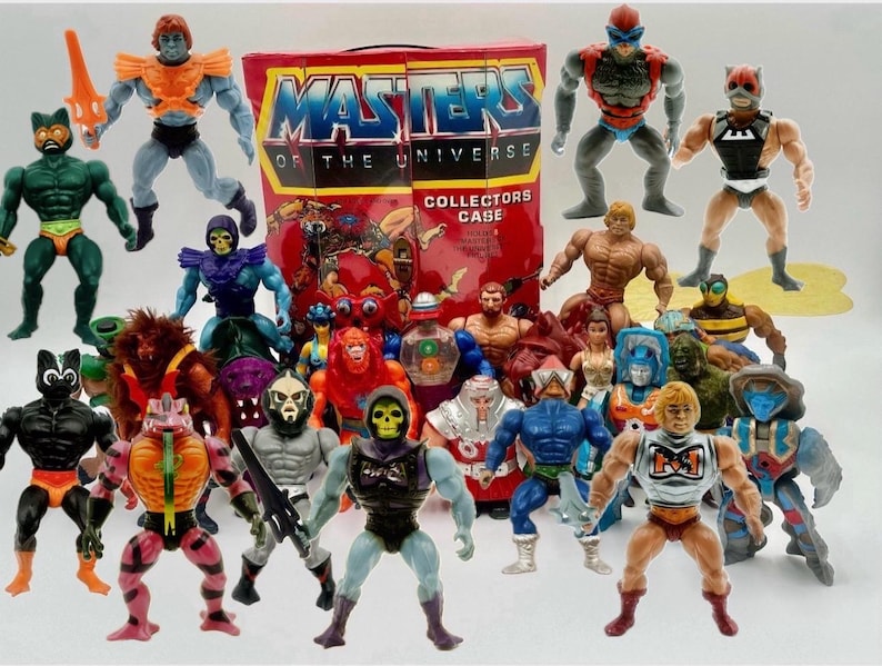 May include: A collection of Masters of the Universe action figures, featuring various characters in vibrant colors. A red box with the words "Masters of the Universe Collectors Case" is visible. The figures are posed in dynamic stances, showcasing their unique designs.