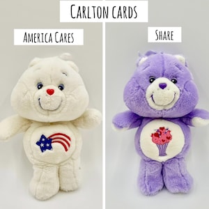 May include: Two Carlton Cards plush toys. The left toy is white with a red, white, and blue star and stripe graphic on its belly and the text America Cares. The right toy is purple with a pink milkshake graphic on its belly and the text Share.