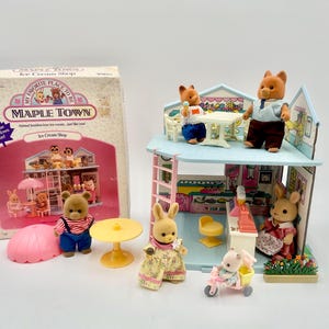 May include: A Maple Town Ice Cream Shop playset with animal figurines. The set includes a two-story building, a box, and several animal figures, including bears and rabbits. The box reads "My Favorite Place to Be" and "Ice Cream Shop".