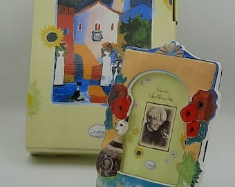 May include: A ceramic picture frame with a colorful design featuring a cat, flowers, and a whimsical archway. The frame has a light blue border and a light orange background. The text "Rosina Wachtmeister" is printed on the frame.