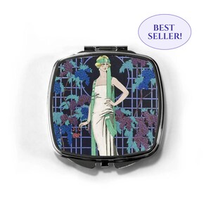 Peut inclure: Un miroir compact argenté avec une illustration vintage d'une femme en robe blanche et foulard vert debout devant un treillis avec des raisins violets. Le miroir a un fond noir et un cadre argenté.
