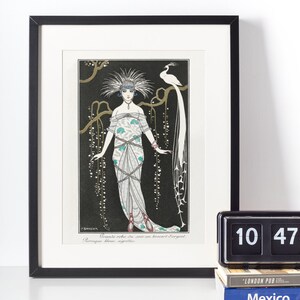 May include: Framed art print featuring an Art Deco illustration of a woman in an elaborate gown with a peacock. The artwork is in black, white, and teal, with the text "Grande robe du soir en brocart d'argent" and "Perruque bleue, angrelles".