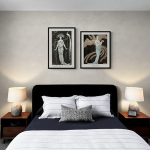 May include: Bedroom interior with a black bed frame, two framed art prints, and two bedside tables with lamps. The bed has white and navy blue bedding with decorative pillows. The art prints feature vintage illustrations in black frames.