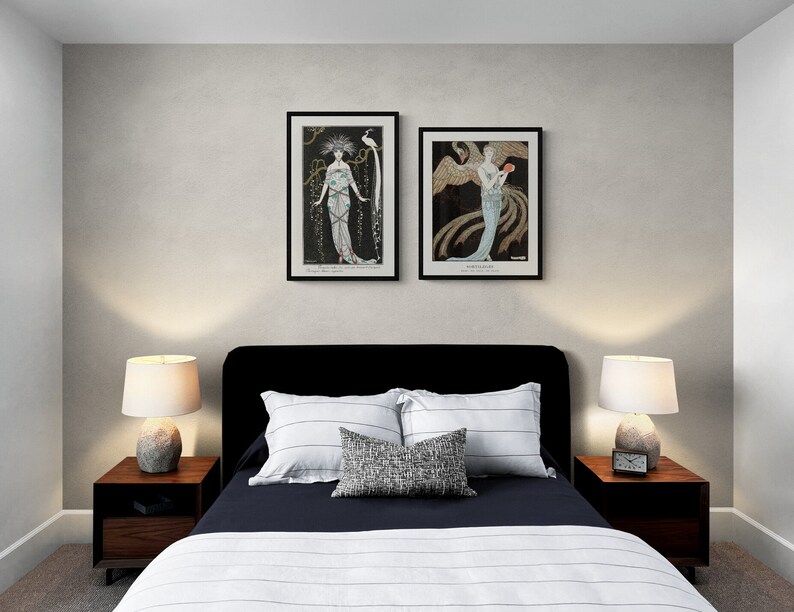 May include: Bedroom interior with a black bed frame, two framed art prints, and two bedside tables with lamps. The bed has white and navy blue bedding with decorative pillows. The art prints feature vintage illustrations in black frames.