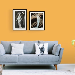May include: Two framed art prints hang above a gray sofa against a yellow wall. The prints feature Art Nouveau illustrations of women with ornate details and dark backgrounds. A striped pillow and a deer pillow decorate the sofa.